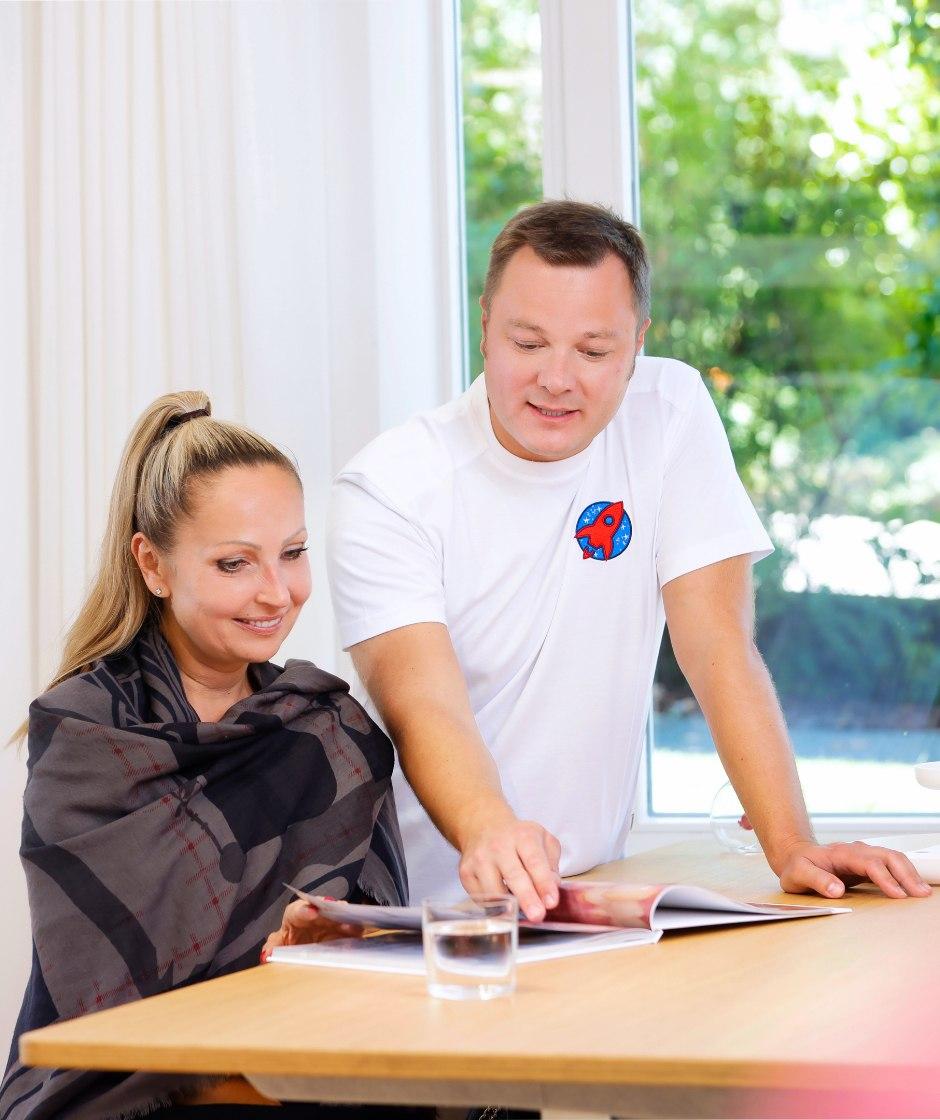 Dr. Sebastian Horvath erklärt einer Patientin ein Bild aus dem Praxisbuch. In diesem Buch sind Behandlungsfälle aus der Praxis Dr. Horvath vorgestellt.