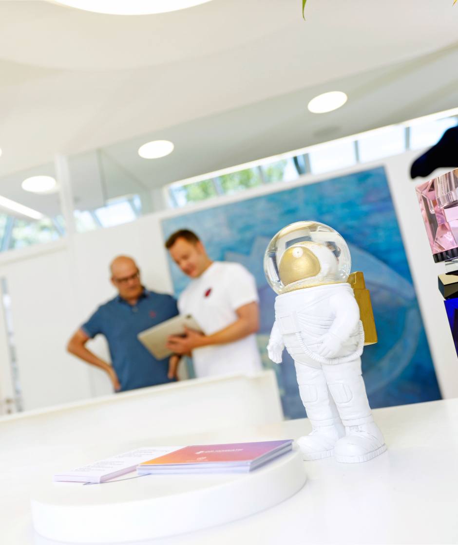 Verschiedene Kunst welche auf der Rezeption ausgestellt ist. Im Hintergrund unterhält Dr. Sebastian Horvath sich mit einem Patienten.