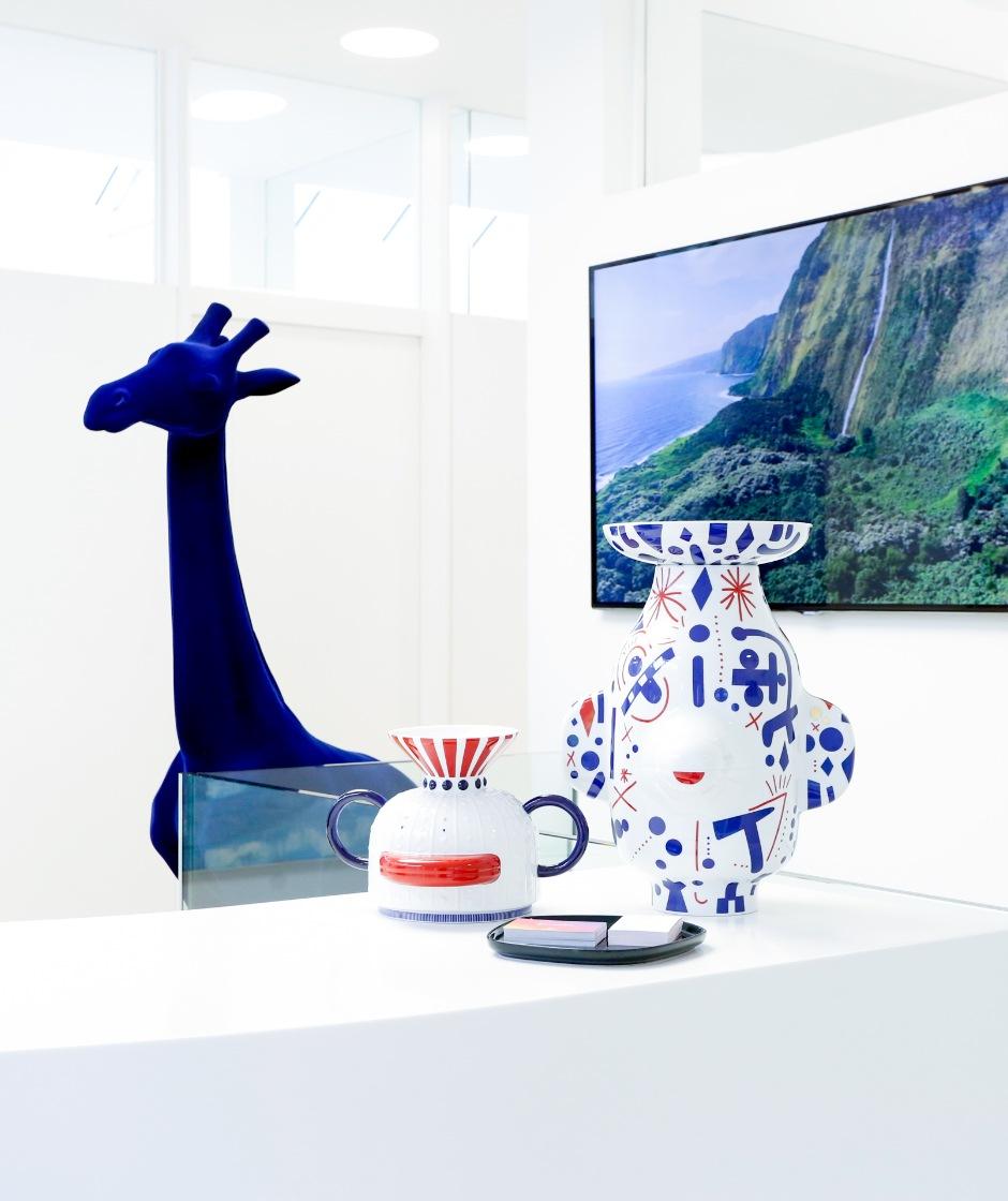 Ausschnitt der Rezeption  auf welcher verschiedene Kunst ausgestellt ist. Im Hintergrund ist ein großes Bild sowie eine Skulptur einer blauen Giraffe.