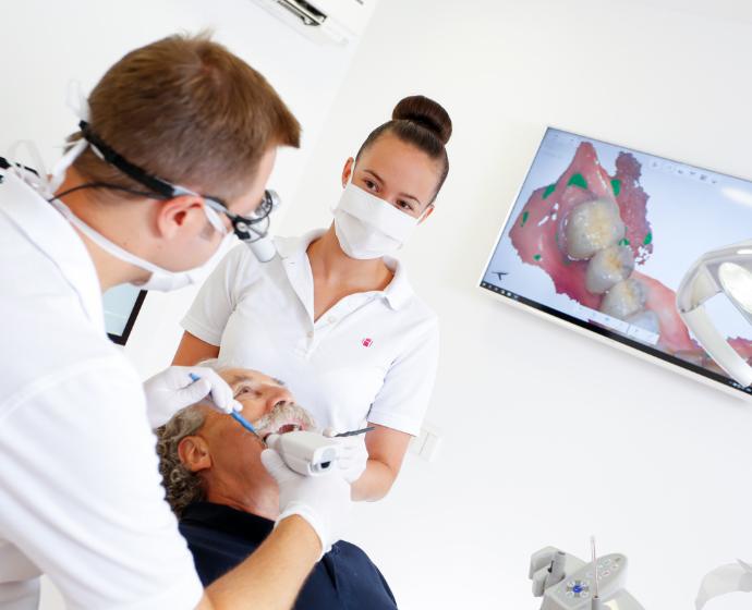 Dr. Sebastian Horvath und eine Assistentin während einer Behandlung an einem Patienten.