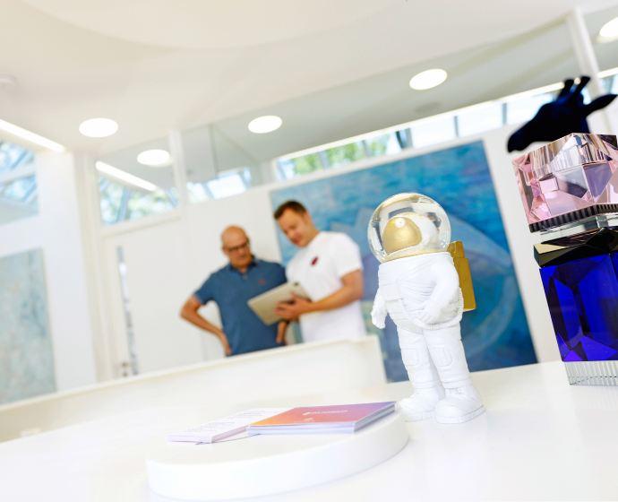 Verschiedene Kunst welche auf der Rezeption ausgestellt ist. Im Hintergrund unterhält Dr. Sebastian Horvath sich mit einem Patienten.