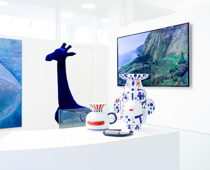 Ausschnitt der Rezeption auf welcher verschiedene Kunst steht. Im Hintergrund ist ein großes Bild sowie eine Skulptur einer blauen Giraffe.
