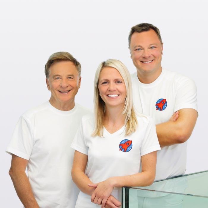 Herzlicher Empfang bei Dr. Horvath: Dieses Bild präsentiert das freundliche und professionelle Team der Zahnarztpraxis, bestehend aus Dr. Nicole Horvath, Dr. Sebastian Horvath und Dr. Domonkos Horvath, alle lächelnd in ihren Praxisuniformen mit dem Praxislogo, bereit, den Patienten die beste Zahnversorgung zu bieten.