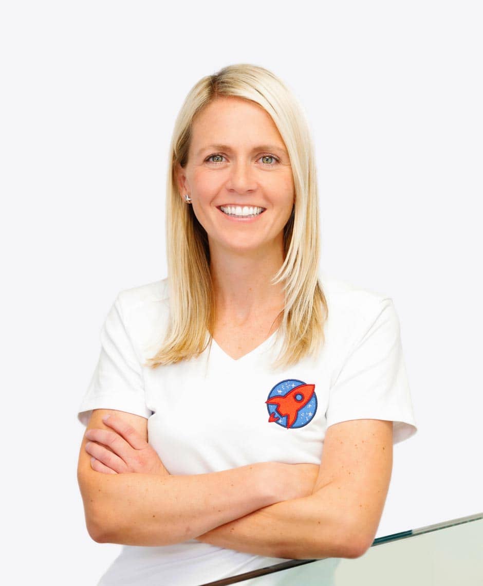 Dr. Nicole Horvath, spezialisiert auf Kieferorthopädie: Ein professionelles Portrait von Dr. Nicole Horvath, die lächelnd und verschränkten Armen vor einer ruhigen, blauen Wasser-Hintergrundkulisse steht. Das Bild verkörpert Vertrauen und Fachwissen, welches Patienten bei der Suche nach einer Expertin für Kieferorthopädie Sicherheit gibt