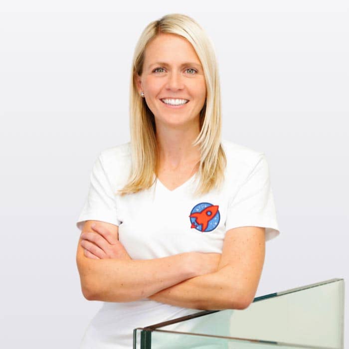 Dr. Nicole Horvath, spezialisiert auf Kieferorthopädie: Ein professionelles Portrait von Dr. Nicole Horvath, die lächelnd und verschränkten Armen vor einer ruhigen, blauen Wasser-Hintergrundkulisse steht. Das Bild verkörpert Vertrauen und Fachwissen, welches Patienten bei der Suche nach einer Expertin für Kieferorthopädie Sicherheit gibt