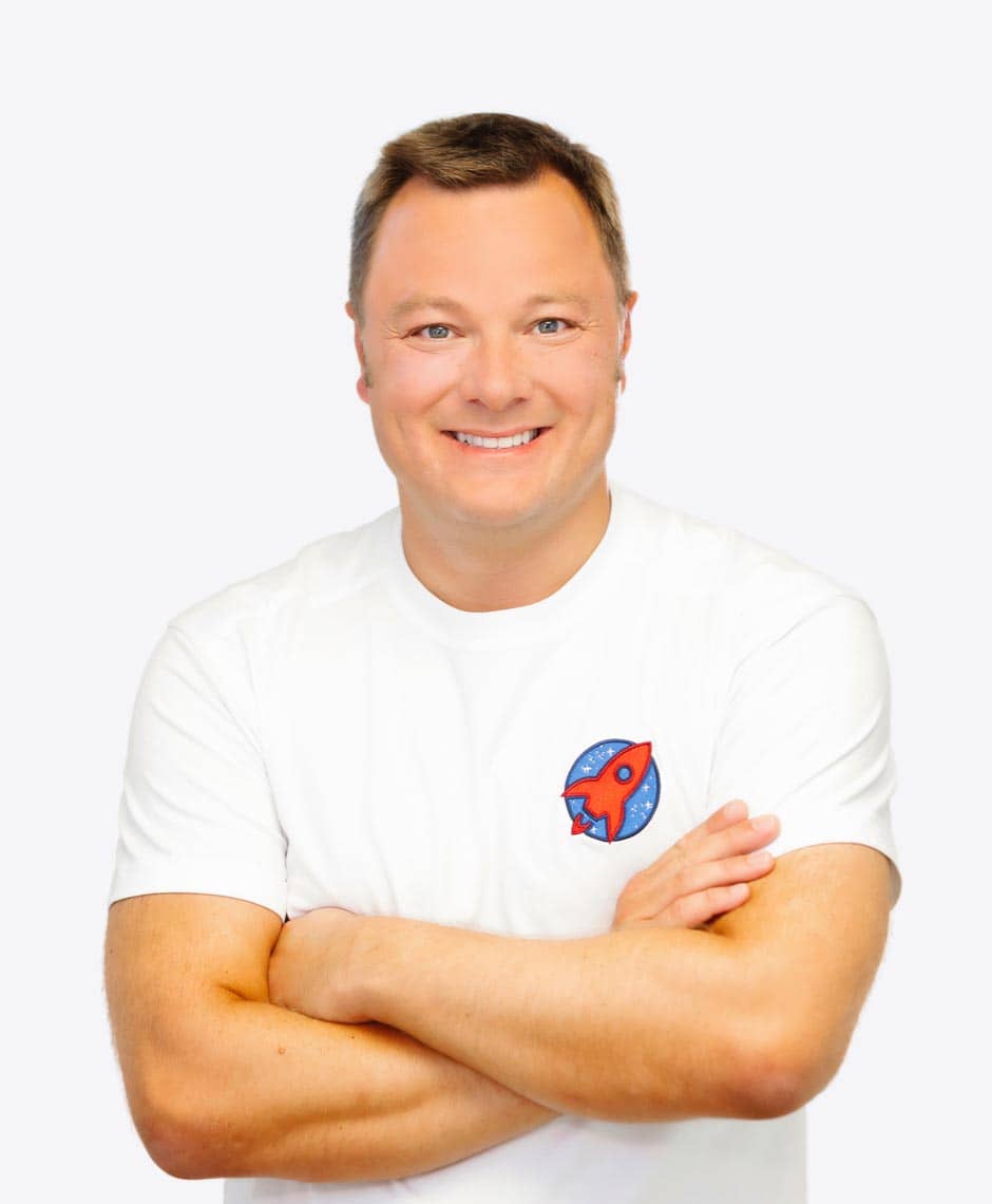 Professionelles Porträt von Dr. Sebastian Horvath, der mit verschränkten Armen lächelt. Seine zuversichtliche Ausstrahlung und das Praxislogo auf seinem T-Shirt repräsentieren das Engagement für exzellente zahnmedizinische Versorgung.