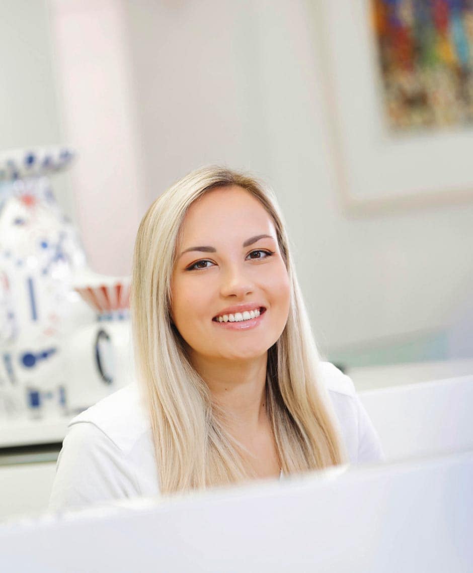 Freundlicher erster Eindruck: Eine herzliche Rezeptionistin begrüßt Patienten an der Rezeption von Dr. Horvaths Praxis. Ihre einladende Haltung verkörpert den Geist des Praxisteams, das sich der Patientenpflege widmet