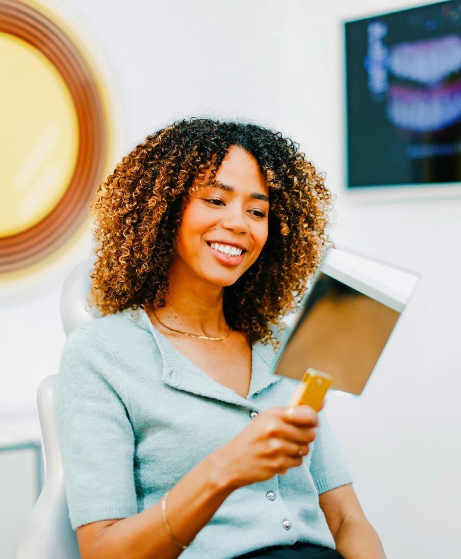 Patientin betrachtet mit Freude ihr Lächeln im Spiegel nach Invisalign-Behandlung in der Zahnarztpraxis Dr. Horvath bei Zürich.