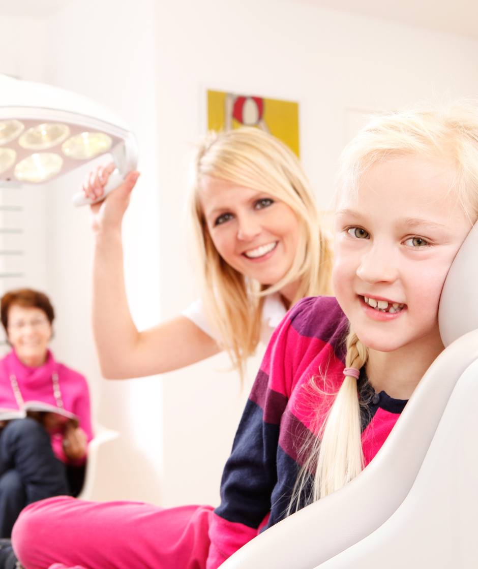 Dr. Nicole Horvath und Ihre Junge Patientin welche gerade auf dem Behandlungsstuhl sitzt lachen freundlich in die Kamera.
