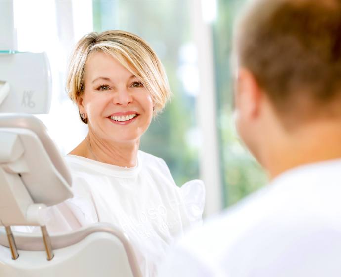 Eine lächelnde Patientin zusammen mit Dr. Sebastian Horvath auf einem Behandlungsstuhl in unserem hellen Behandlungszimmer vor einem Fenster.