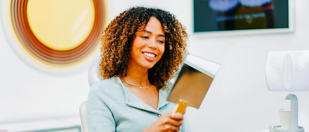 Patientin betrachtet ihr neues Lächeln nach ästhetischer Zahnsanierung zufrieden im Spiegel